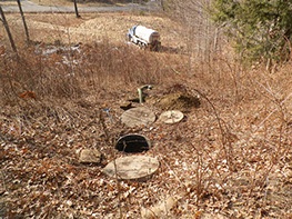 Sewer in wooded area with Henniker Septic truck in the background located in New Hampshire.